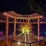 A beautifully lit up flower arrangement is displayed under a wooden structure.
