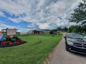 A black car is parked on a gravel road in front of a house.