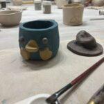 A blue and yellow cup sits on a table next to a red hat.