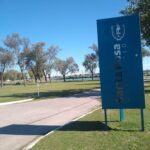A blue sign with white lettering is standing in a grassy field.