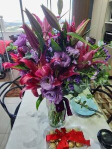 A bouquet of flowers sits on a table, with a box of chocolates nearby.