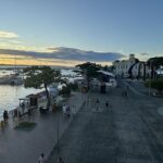 A busy street with people walking and boats in the water.