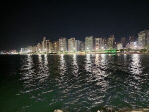 A city skyline is lit up at night, with a large body of water in the foreground.