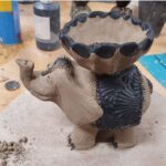 A clay elephant statue is displayed on a wooden table.