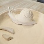 A clay sculpture of a snail is sitting on a plate.