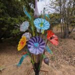 A colorful glass flower arrangement is displayed in a garden setting.