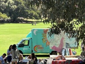 A colorful truck with a painting of a farmer on the side is parked in a field, surrounded by people.