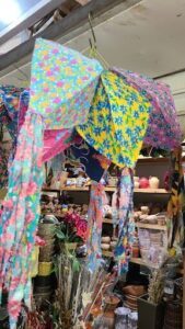 A colorful umbrella hangs over a table filled with various items, including vases and a potted plant.