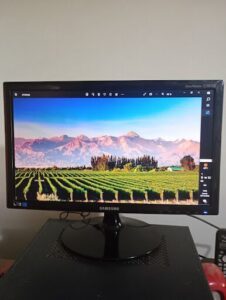 A computer monitor displays a beautiful mountain scene with a vineyard in the foreground.