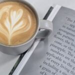 A cup of coffee sits on a book, with a heart-shaped foam on top.