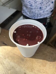 A cup of red liquid with white specks in it sits on a table.