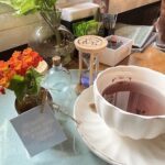 A cup of tea sits on a table next to a vase of flowers.