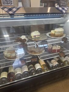 A display case filled with various desserts and bottles of wine.
