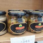 A display of jars of food, including pickles and olives, with a price tag of $3.45.