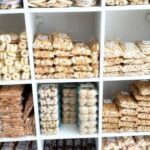A display of various pastries, including donuts and cookies, is arranged on shelves in a bakery.