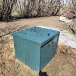 A green box sits in a field, surrounded by trees and dirt.