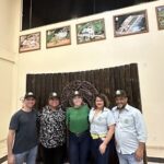 A group of five people pose for a picture in front of a wooden structure.