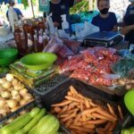 A group of people are gathered around a table filled with various fruits and vegetables.