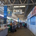 A group of people are gathered in a market, with a sign above them that reads "latinos."