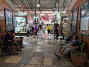 A group of people are walking down a hallway in a marketplace, with some sitting on benches and others standing.