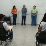 A group of people, including a man and two women, are standing in front of a whiteboard.