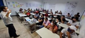A group of people wearing face masks are sitting in a classroom, attentively listening to a presentation.