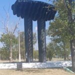 A large black sculpture of two pillars stands in a park.