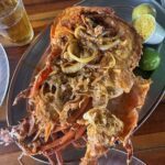 A large cooked lobster with onions and a beer in the background.