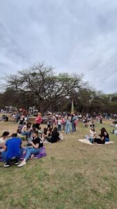 A large group of people are gathered in a park, enjoying a sunny day.