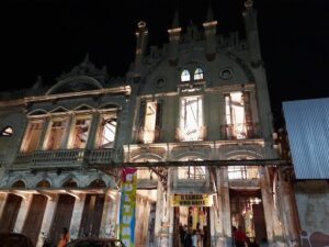 A large, old building with a clock tower and a sign that says "Poder Vira Bail" stands in the night.