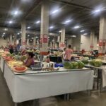 A large room filled with tables and people selling fruits and vegetables.