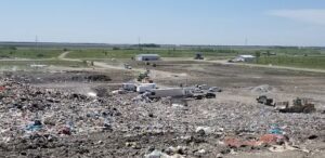 A large trash heap is filled with garbage, including a white truck, and is located in a field.