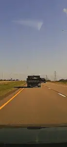 A large truck is driving down a highway, with a car following behind it.