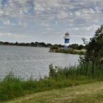 A lighthouse stands tall on a grassy hill overlooking a body of water.