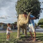 A man and a little girl are standing next to a statue of an elephant.
