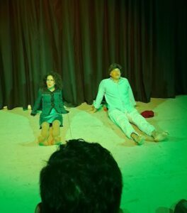 A man and a woman are sitting on the floor, with the man on his knees and the woman sitting on the floor next to him.