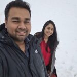 A man and woman are standing in the snow, smiling and enjoying the winter weather.