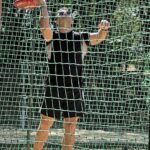 A man in a black shirt and shorts is reaching up to catch a frisbee.