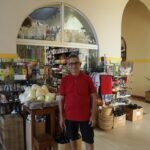 A man in a red shirt stands in front of a store filled with various items.