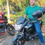 A man is sitting on a motorcycle, smiling and holding a black helmet.