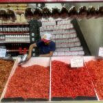 A man is standing in front of a table full of red peppers.