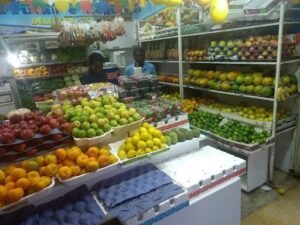 A man stands in front of a fruit stand, surrounded by a variety of fruits.