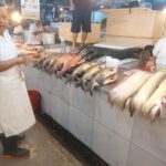 A man stands in front of a table filled with fish, smiling and enjoying the moment.
