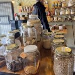 A man stands in front of a table filled with various jars of food, including cookies and cereal.