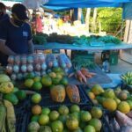 A man stands near a table filled with various fruits and vegetables.