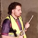 A man wearing a yellow vest is holding a metal pipe.