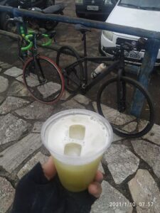 A person is holding a cup of a green drink, possibly a smoothie, while standing next to a bicycle.