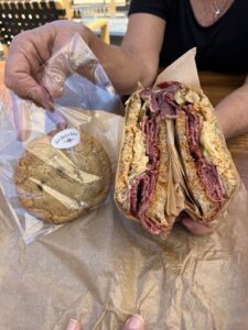 A person is holding a sandwich and a cookie.