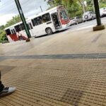 A person is sitting on a sidewalk near a bus stop.