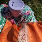 A person is sitting on the grass with a cup of coffee and a spoon.